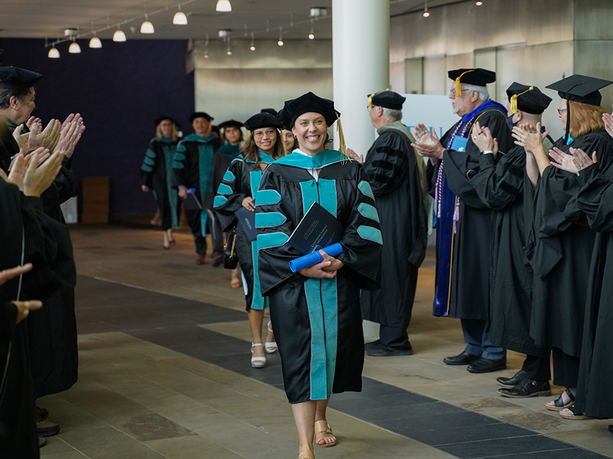 ATSU graduates walking together and smiling while getting a standing ovation from those surrounding them