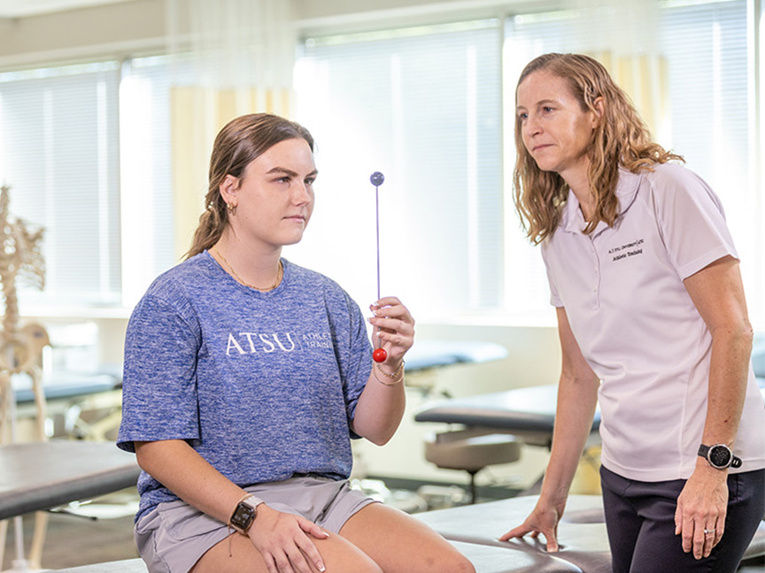 ATSU student performing an exercise with an object in front of her face, assisted by another student