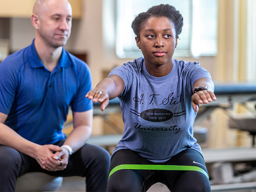 ATSU DAT trainer assisting a client with a squat exercise using a resistance band