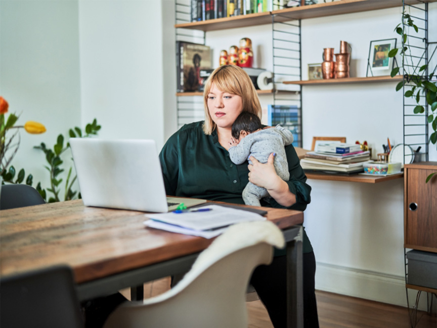 MEd student holding her baby at home while working on her computer, showcasing the online format flexibility of the MEd program.