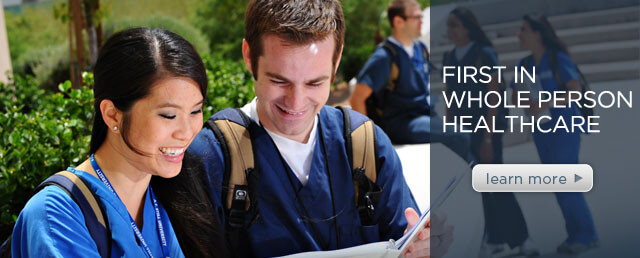 Two medical students dawning scrubs, each smiling while reviewing information in a binder.